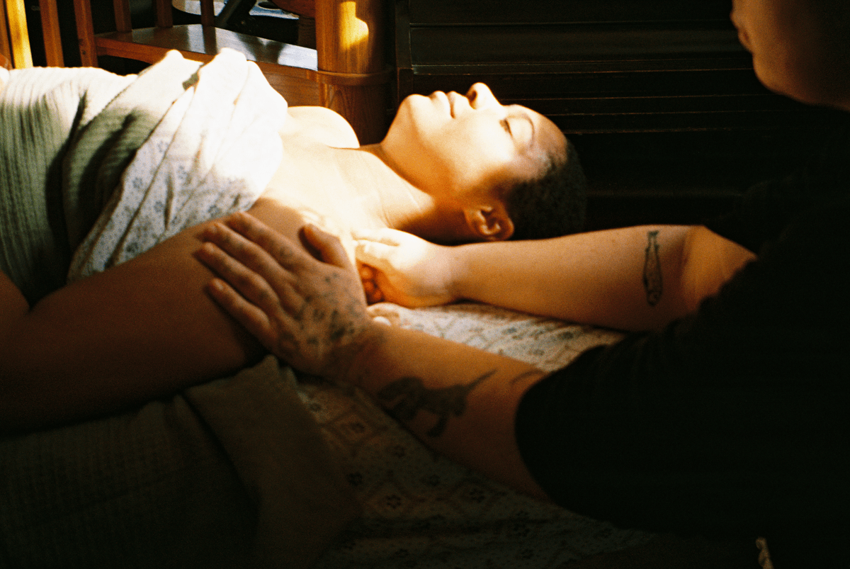 A woman lying down with her eyes closed, receiving a massage from a person with tattoos on their arms.