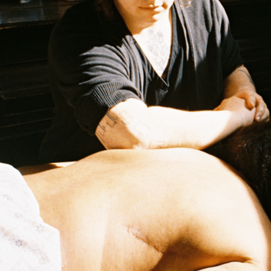 A person giving a massage to another person lying face down, in a setting with wooden walls.