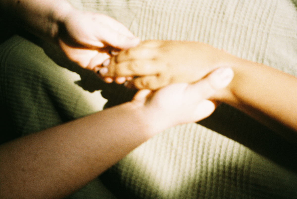 Two hands holding and supporting a person's forearm, with a beige textured fabric in the background.