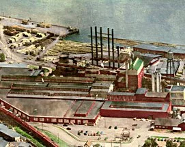 Aerial view of an industrial port with warehouses, docks, and cargo ships by the water.