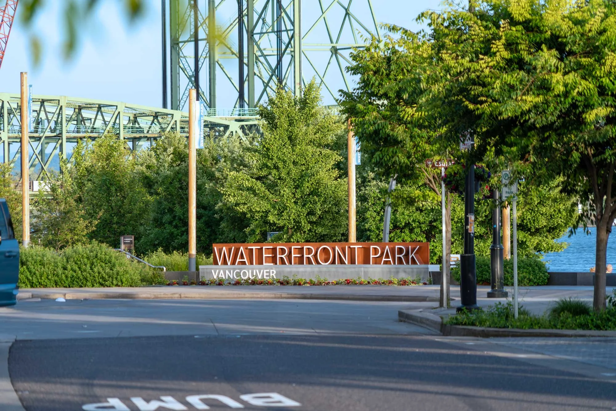 View of Waterfront Park in Vancouver with a large sign, trees, and part of a bridge or tower structure in the background.
