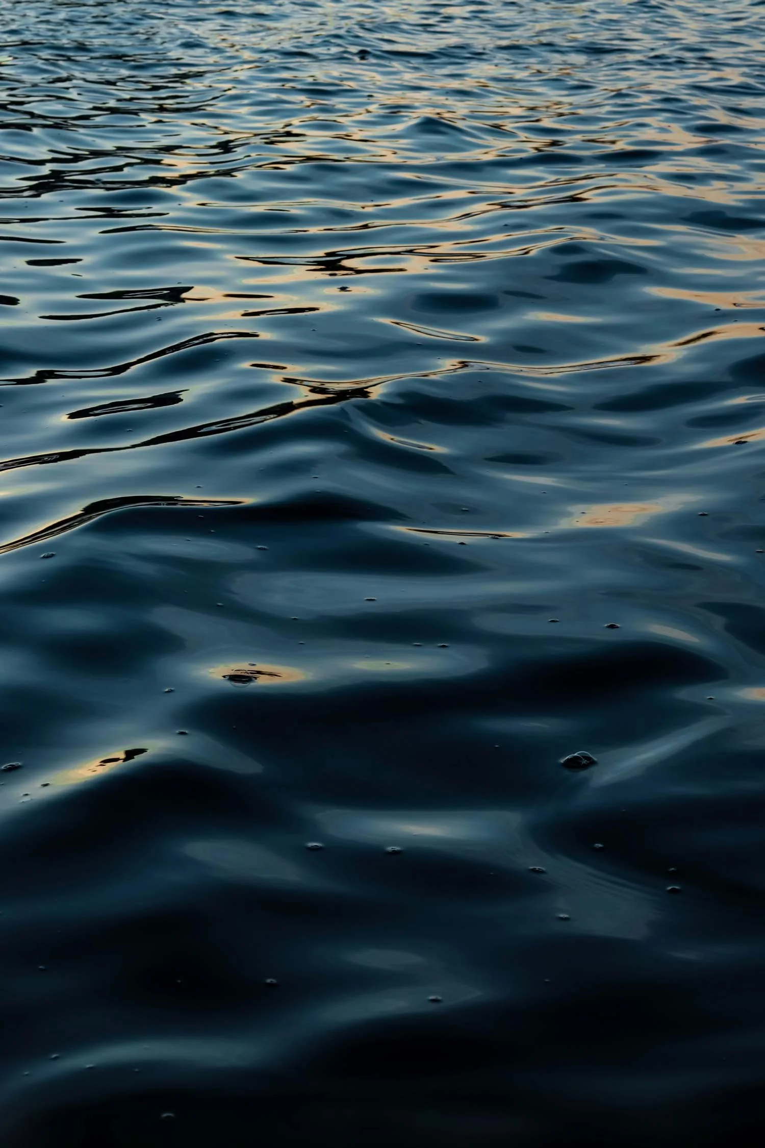 Calm water surface with gentle ripples and reflections of the sky, possibly during sunset or sunrise.