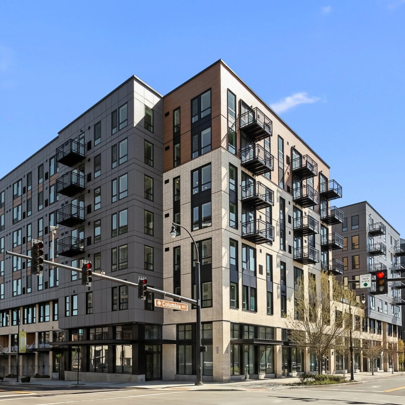 Modern multi-story apartment building at a street corner with balconies and large windows, traffic light, and street sign reading 'Columbia St'
