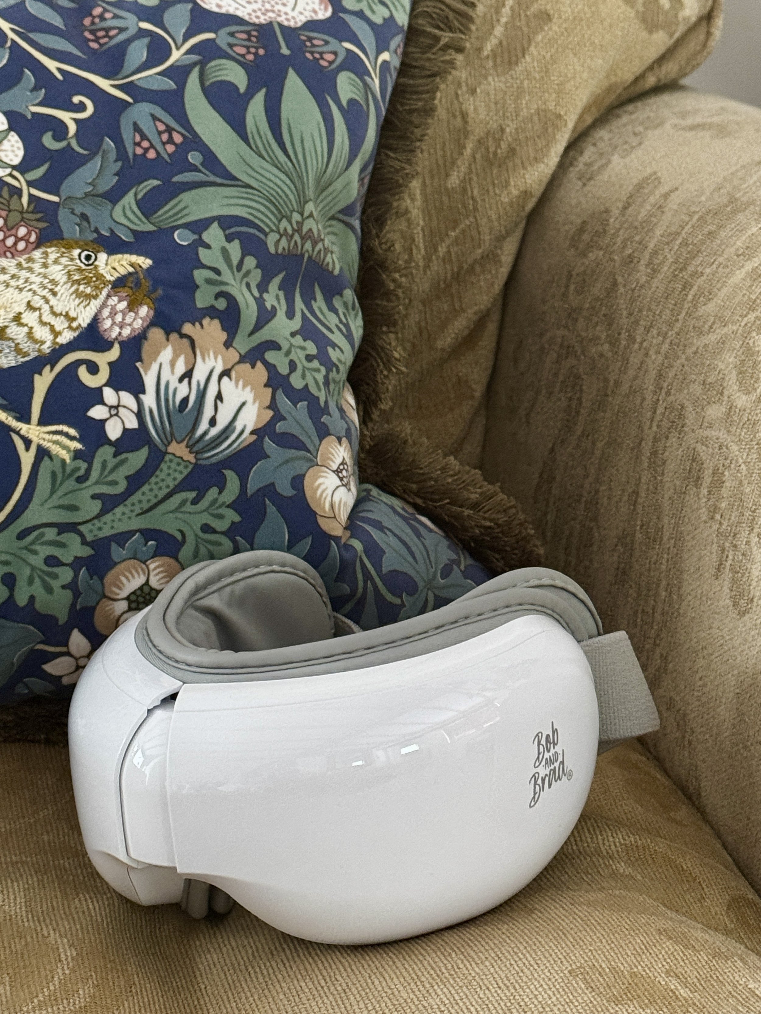 A white baby swing with the words 'Bob and Brenda' written on it, placed on a brown sofa with floral and patterned cushions.