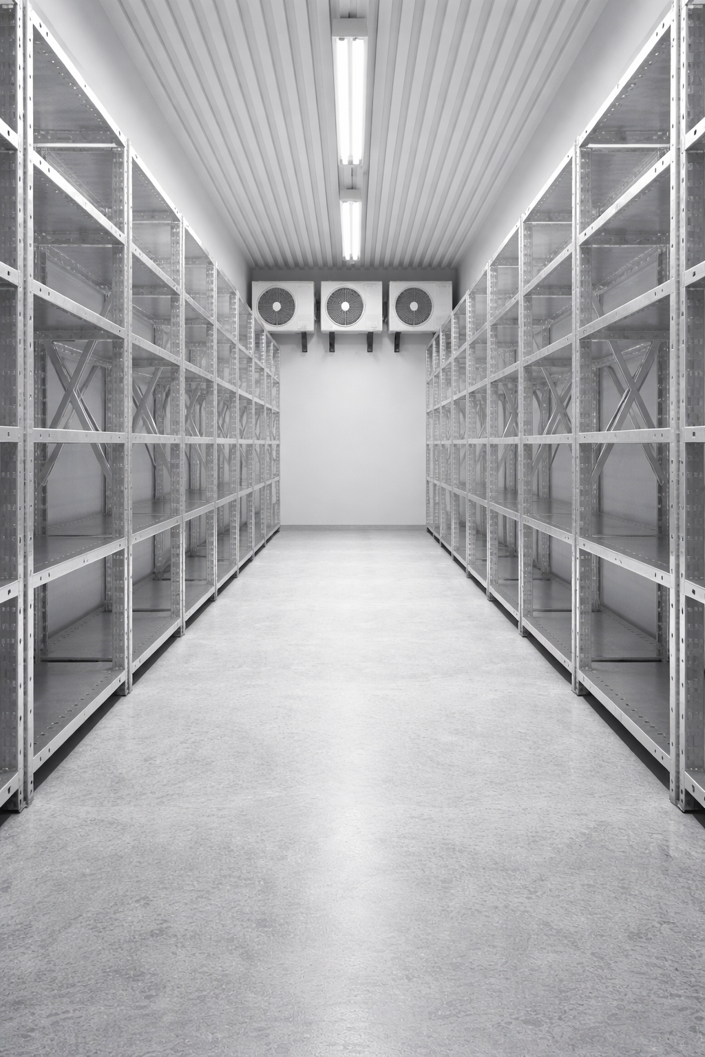 Allée vide avec étagères métalliques et ventilateurs de refroidissement au fond, éclairée par des luminaires au plafond.