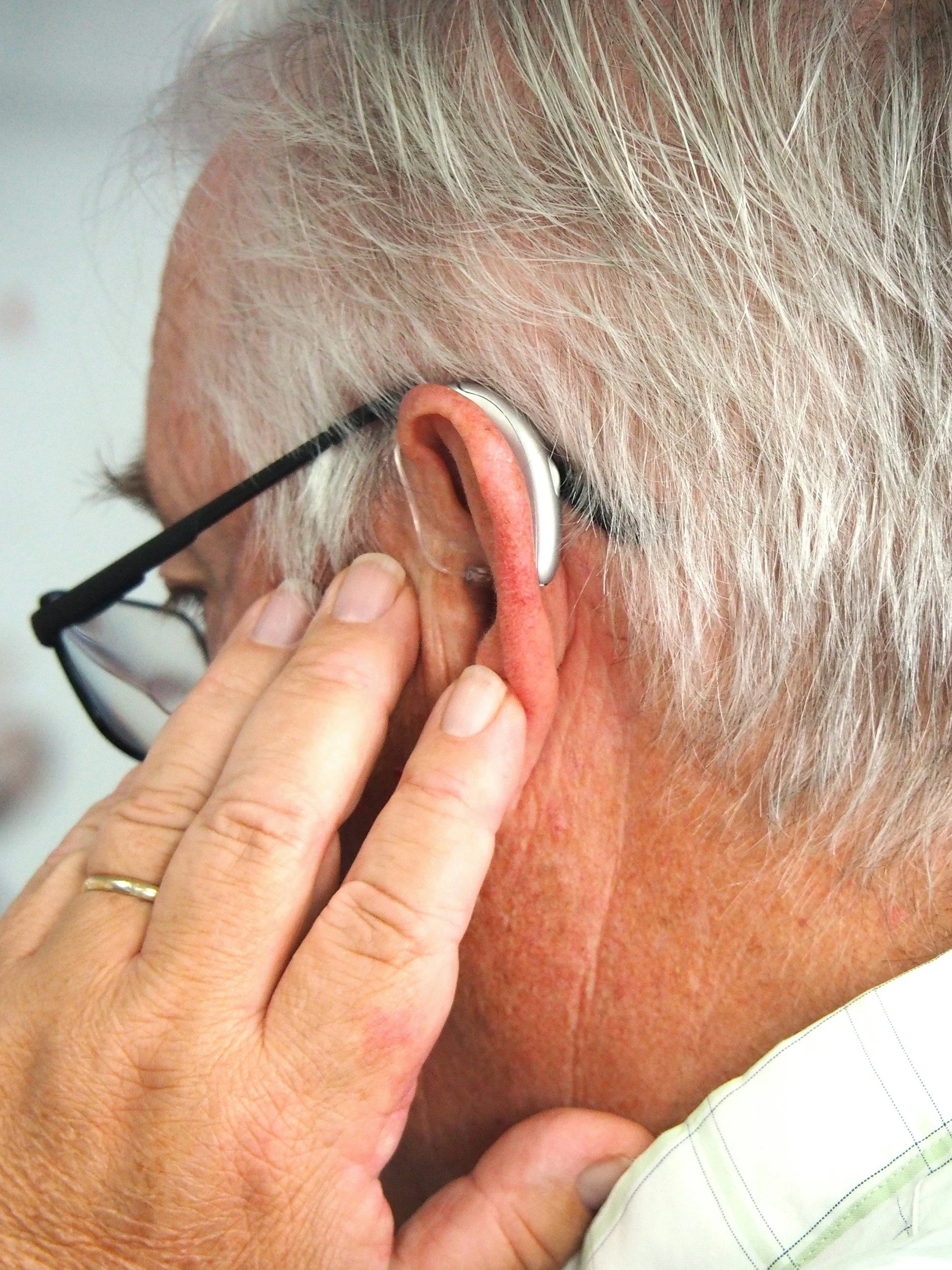 Une personne âgée porte un appareil auditif et a un professionnel qui ajuste ou inspecte son oreille.