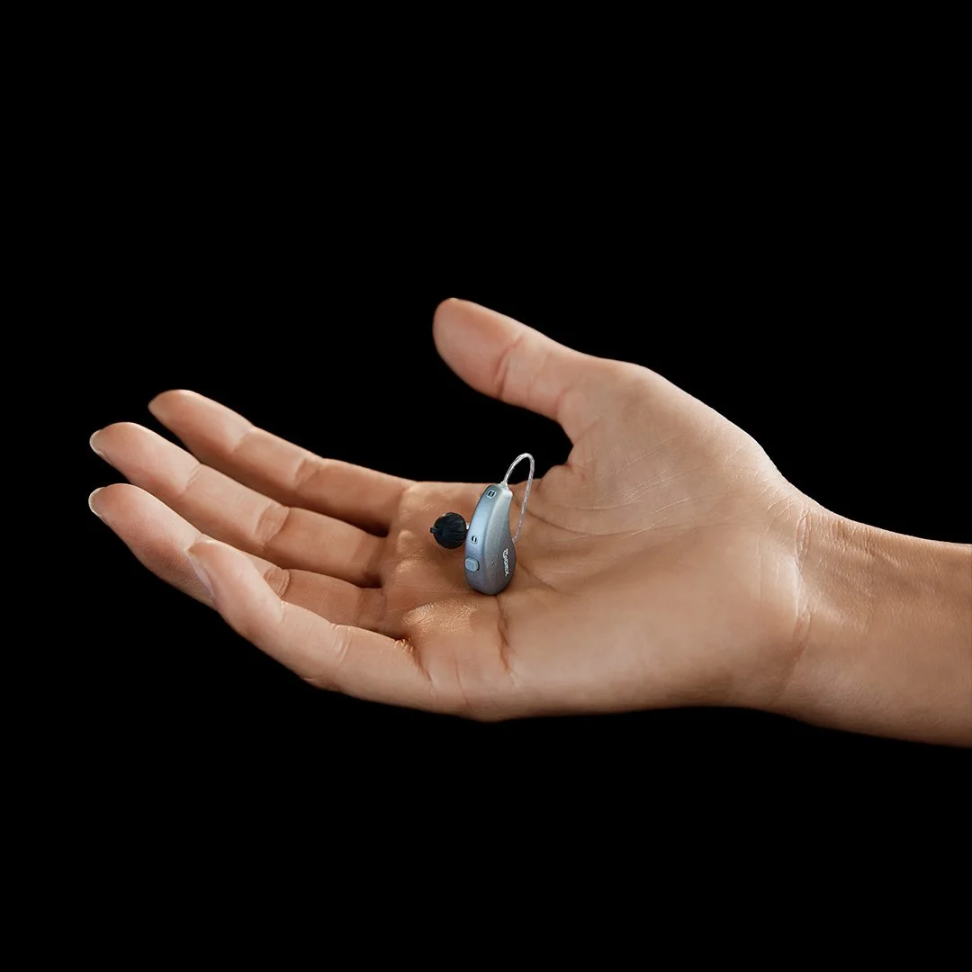 Une main tenant un appareil auditif contre un fond noir.