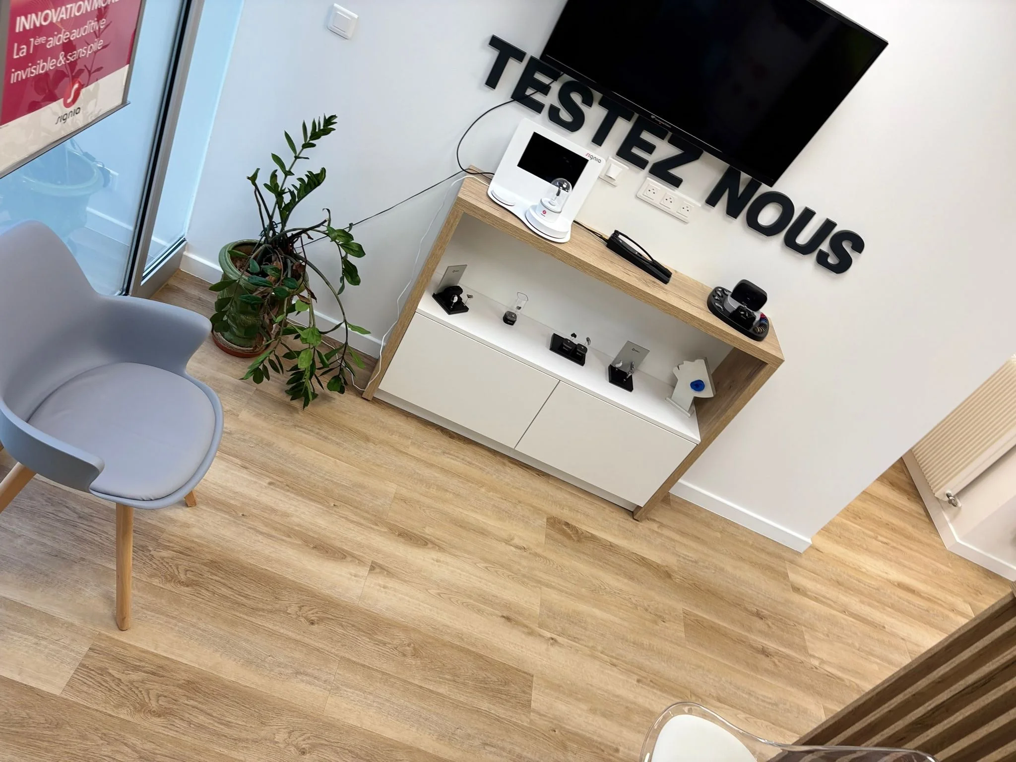 Espace de test avec un grand écran TV, une console, appareils électroniques, une plante verte, un fauteuil gris clair, et des lettres en haut disant « TESTEZ NOUS ».