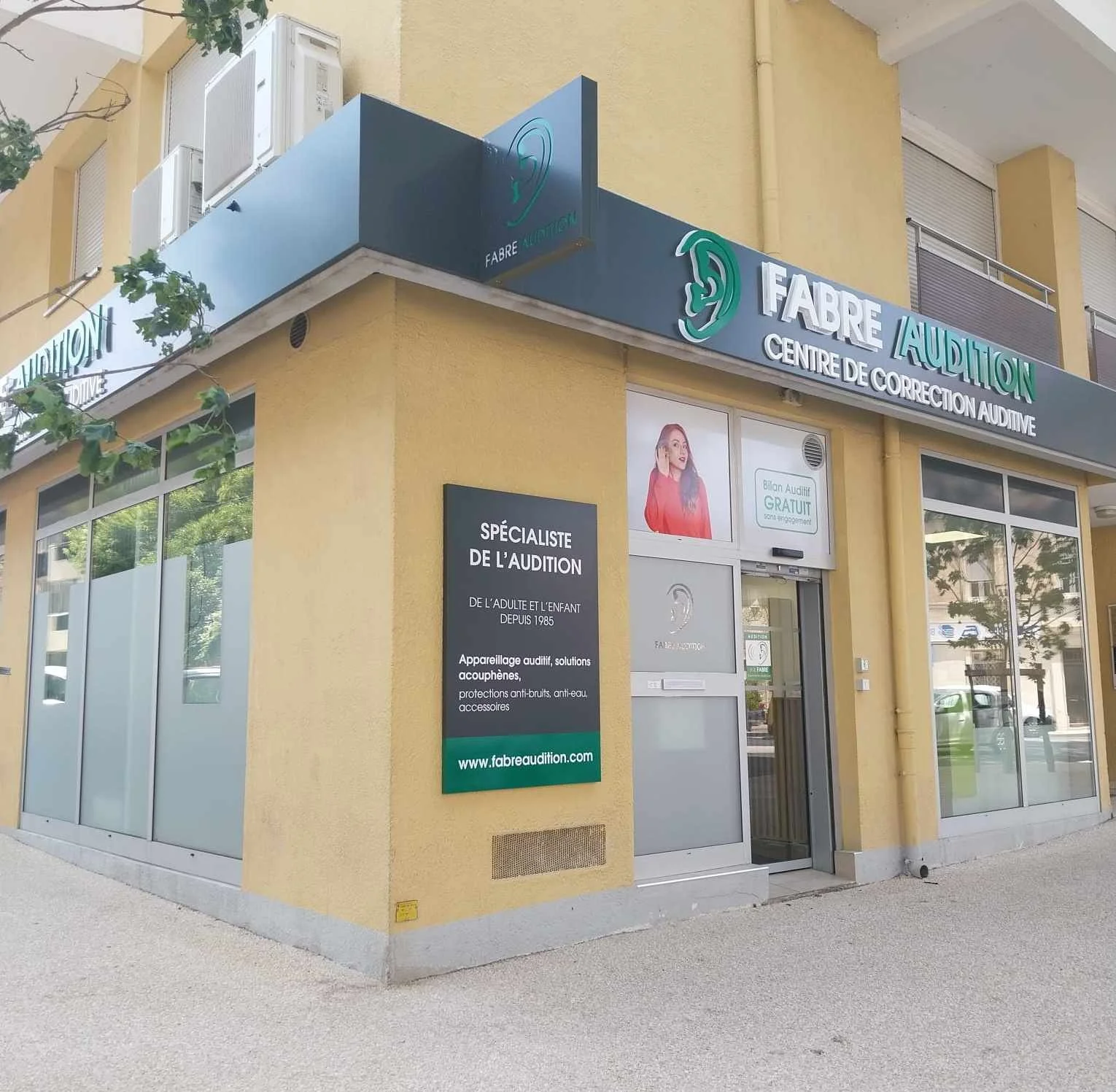 Facade d'un centre d'audition avec signalétique et panneau informatif, bâtiment jaune avec grandes fenêtres.