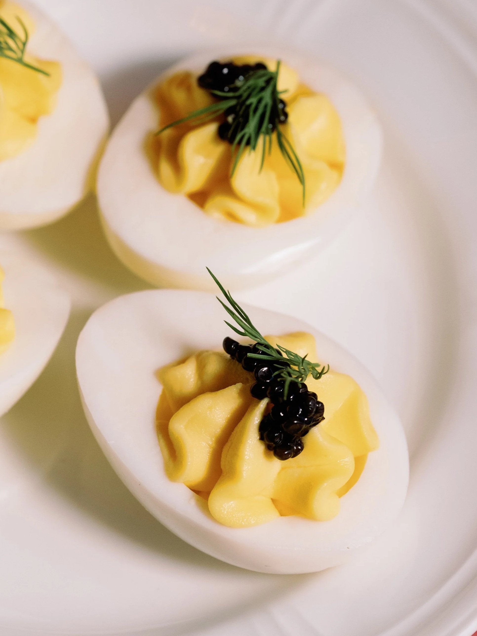 Hard boiled eggs topped with yellow potato salad or mousse, garnished with black caviar and green herbs, served on a white plate.
