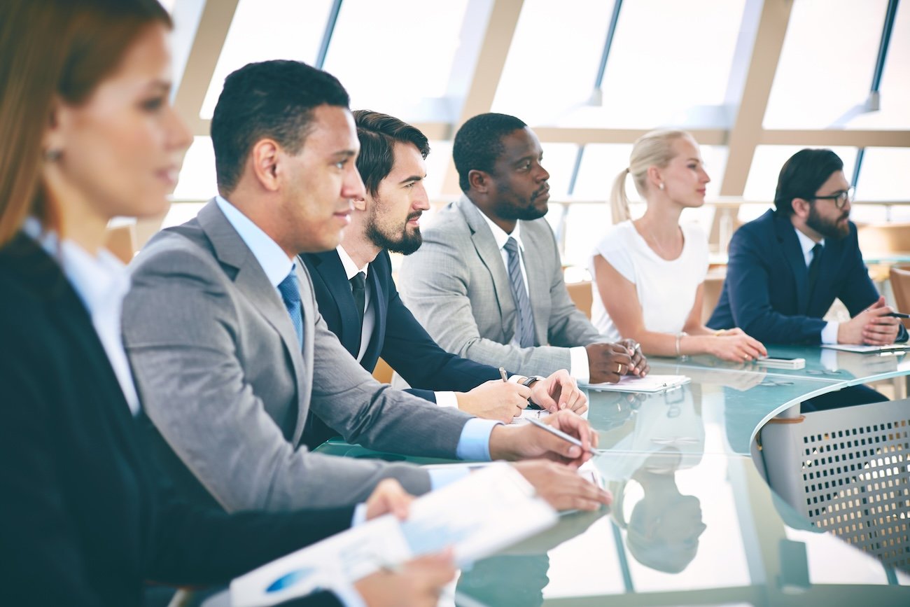 Business professionals attending a meeting in a modern office with large windows.