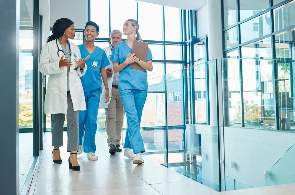 Group of healthcare providers walking in a modern hospital hallway with clipboards.   
