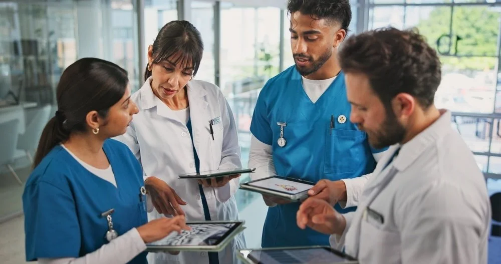 Four medical providers,  gathered around discussing and looking at electronic records on tablets in a modern clinic..