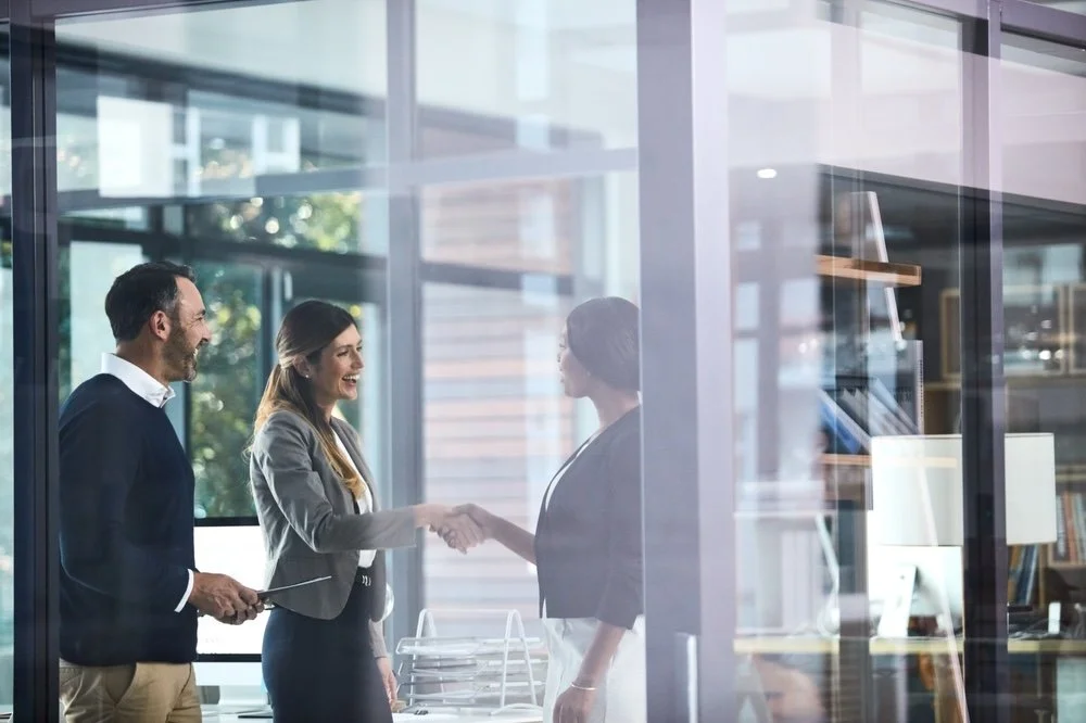 Healthcare IT leaders shake hands inside a modern glass office.