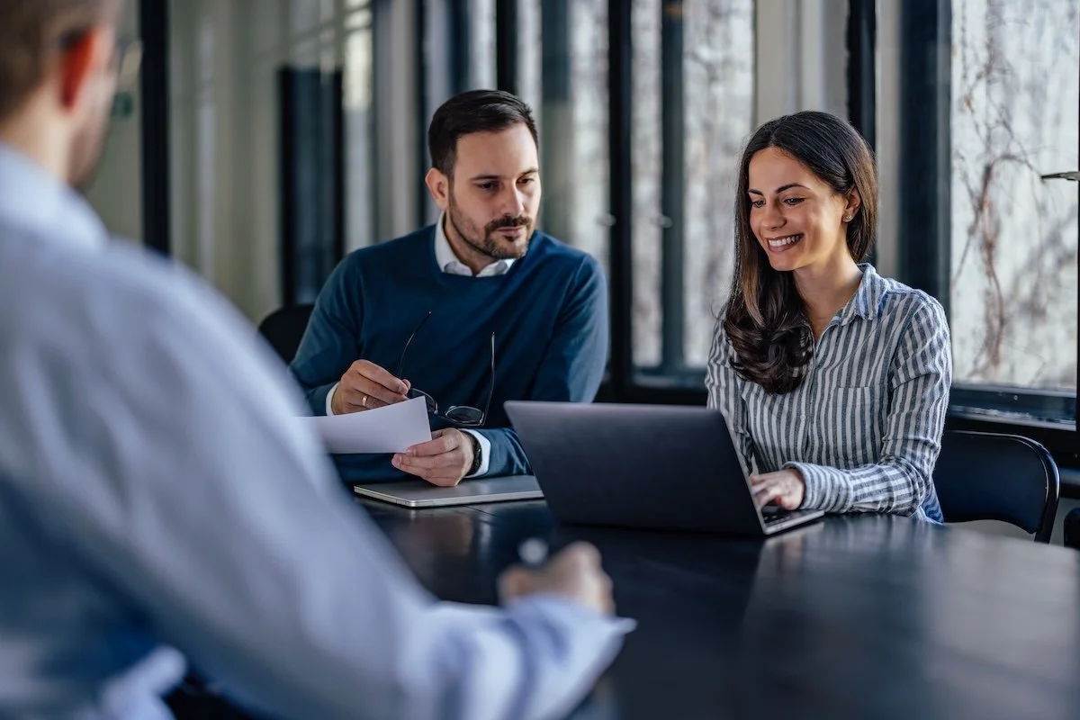 Three healthcare IT consultants in a meeting room having a discussion about epic refuel support, sitting at a table with laptops and papers.