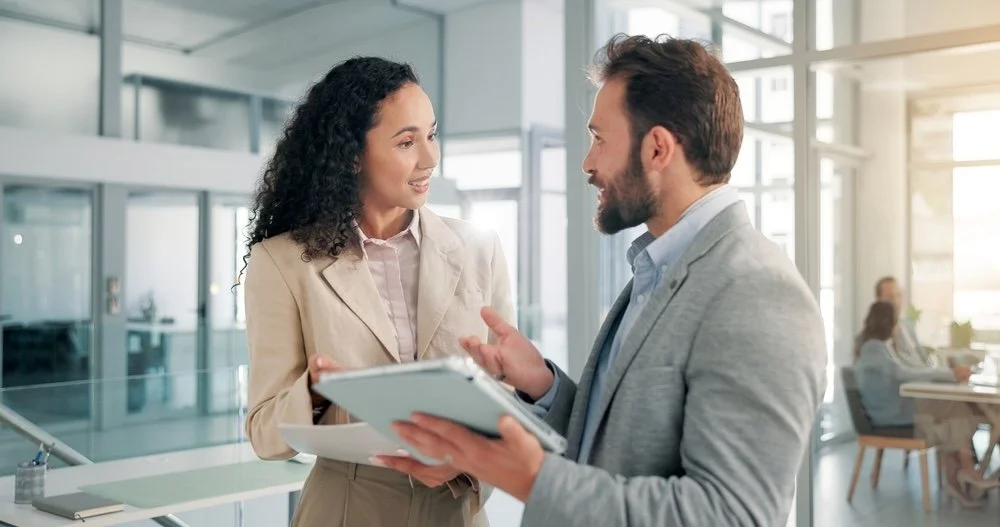 Healthcare IT businesswoman and businessman having a conversation in an office,  holding documents on regarding data accuracy.