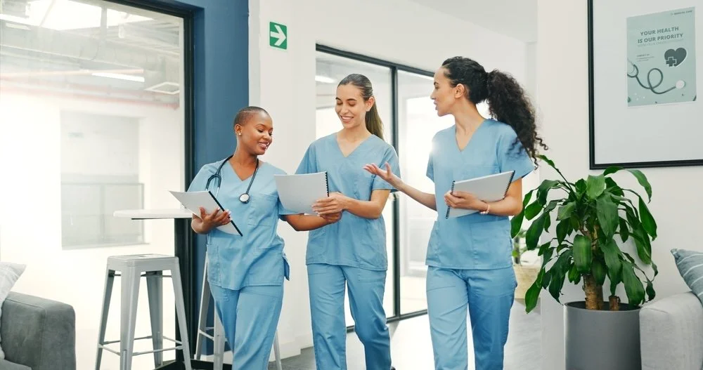 Three nurses walking in hospital hallway sharing data and notes, supporting patient care.
