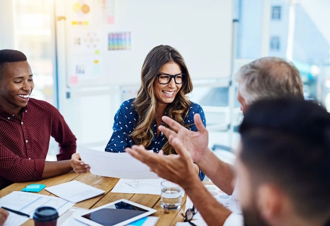 Four diverse healthcare IT leaders having a discussion around a table about epic community connect program in a bright office.