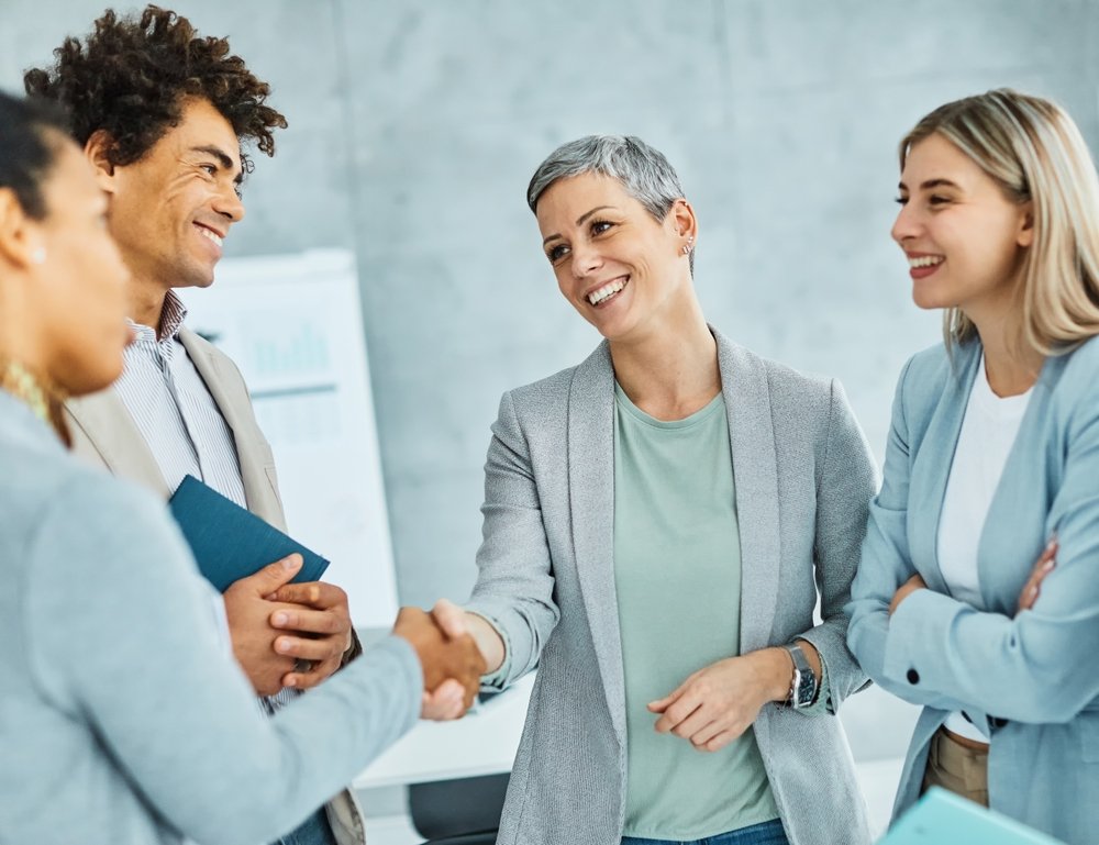 A group of professionals in a business setting, smiling and engaging in a handshake and career conversations.