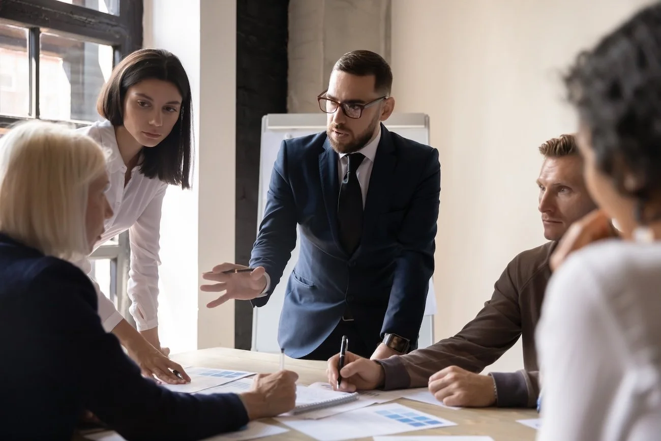 Group of five diverse business professionals having a discussion around a table in a modern office.
