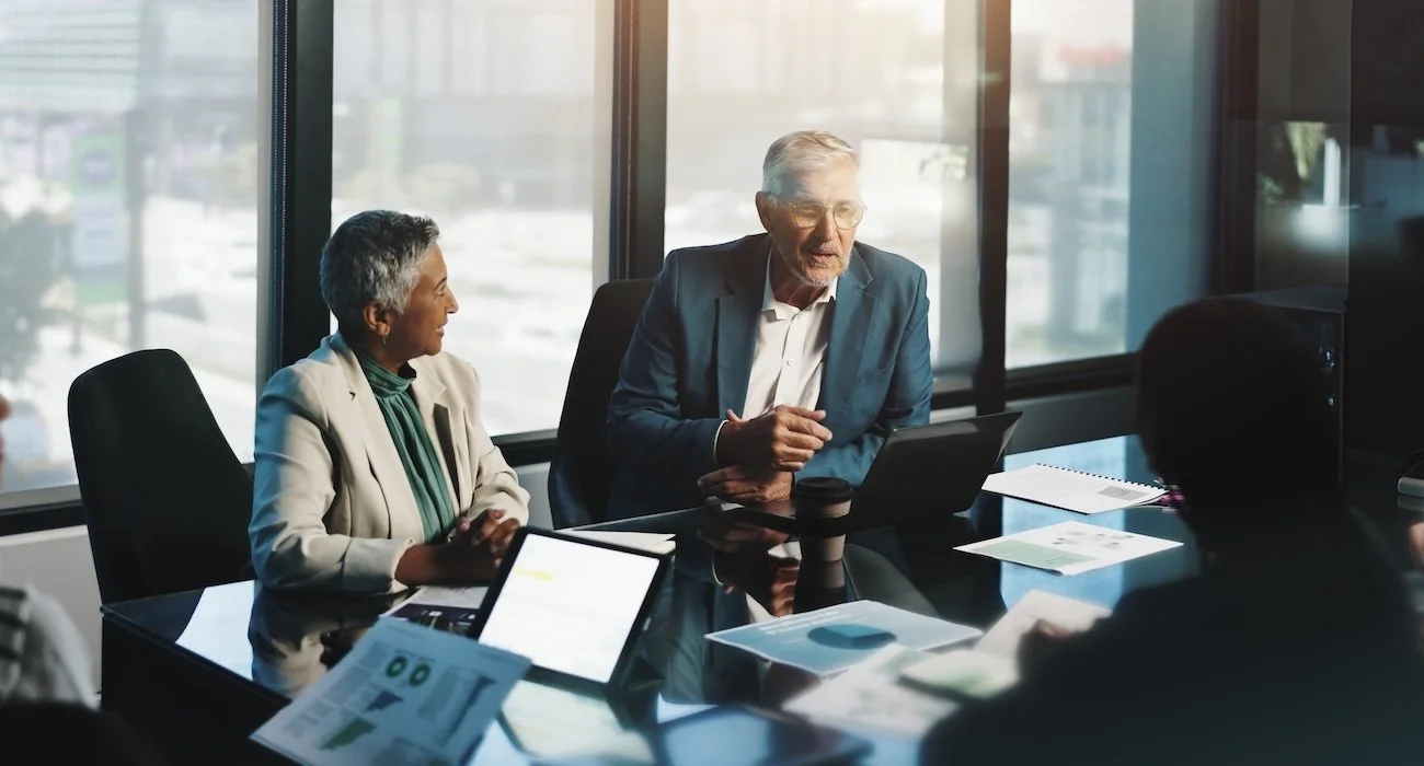 Business meeting with four healthcare executive leaders in a conference room, engaging in a discussion with documents and laptops on the table.
