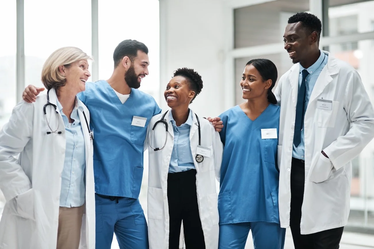 Group of five healthcare professionals, including doctors and nurses, smiling and walking together in a hospital hallway.