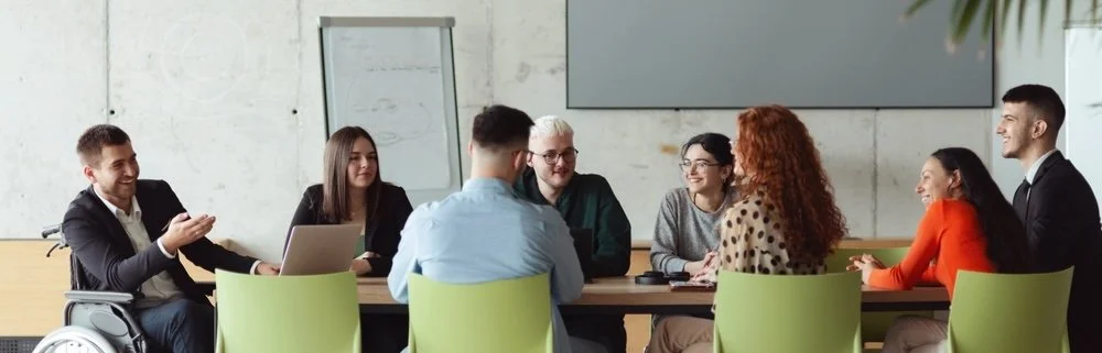 Group of eight diverse young professionals sitting around a conference table during a meeting in a modern office.