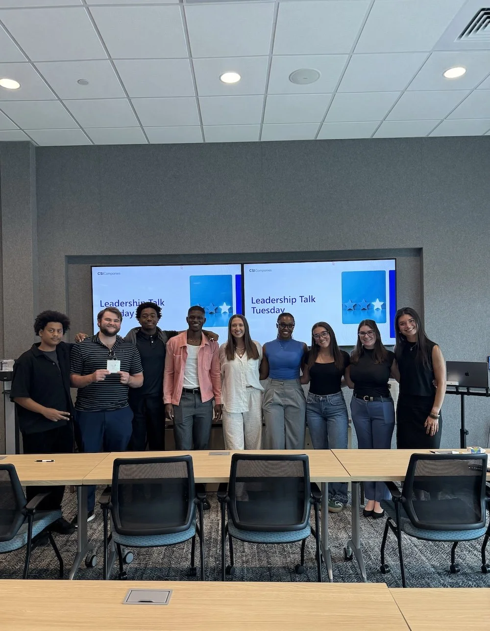 A group of CSI Connect interns standing in a conference room, smiling, with two screens in the background displaying 'Leadership Talk Tuesday'.
