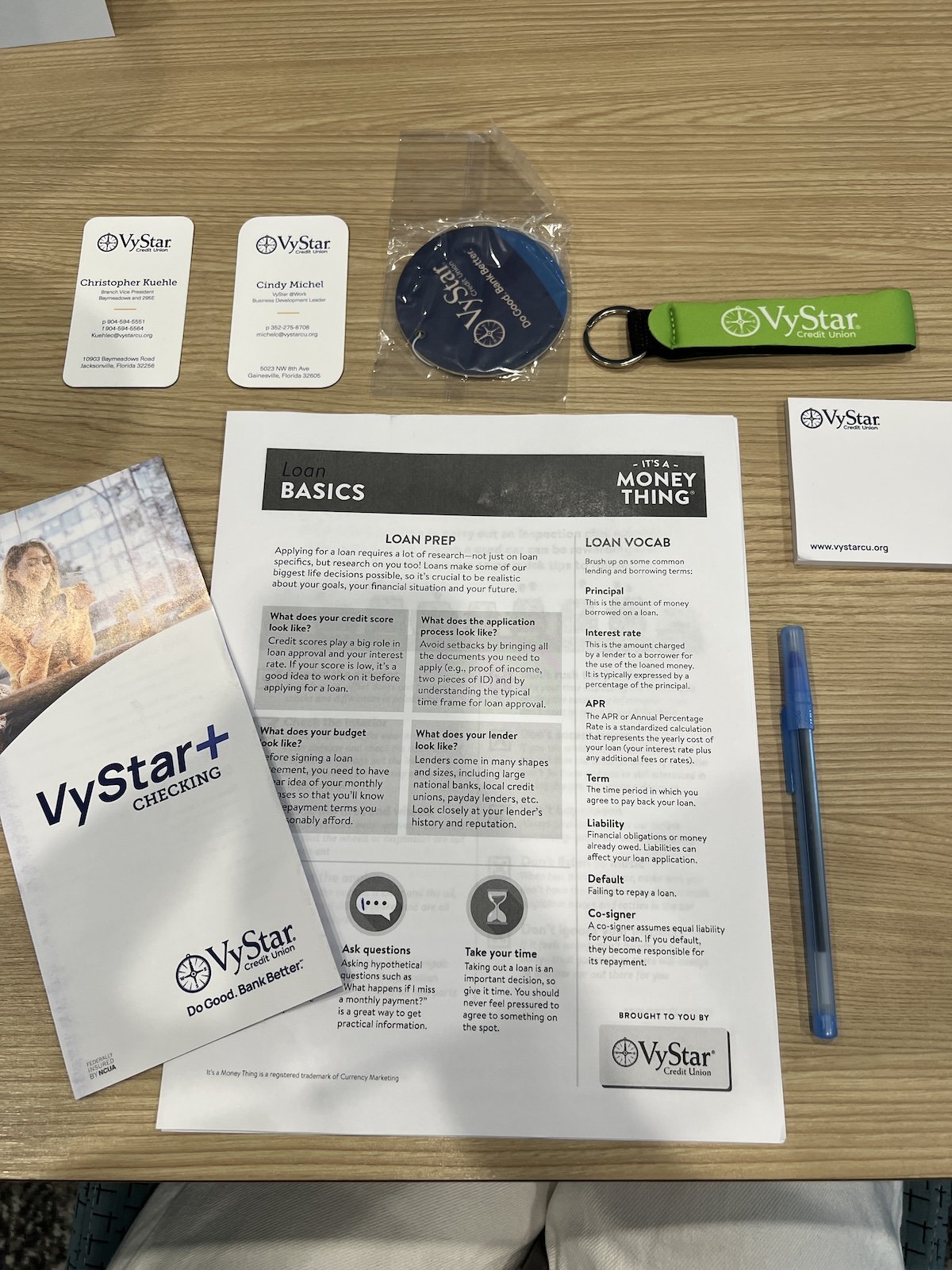 Business cards, a keychain, a round badge, a printed informational sheet about loans, a folded brochure on financial literacy, showcasing Vystar bank visiting CSI connect interns to educate students on tools to secure a quality financial future.