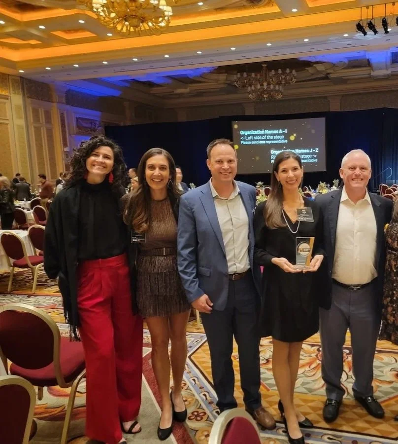CSI leadership team standing in a banquet hall, with chairs and a presentation screen in the background, celebrating an award achievement winning best in KLAS.