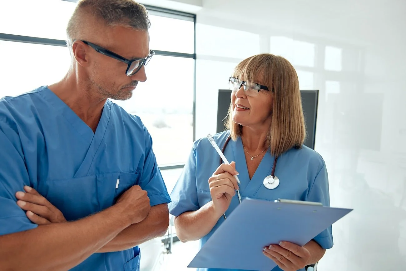 Woman and man healthcare providers, discussing patient care and clinical documentation integrity in a hospital meeting room.