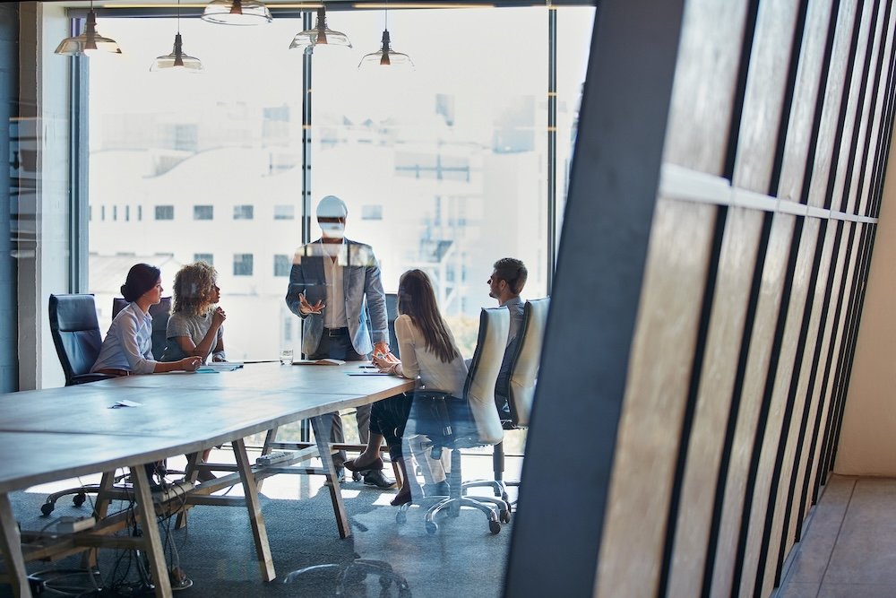 Business meeting in a modern conference room with five healthcare IT leaders, seated around a large table and talking.