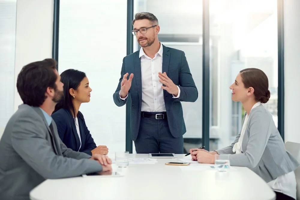 Healthcare IT consultant talking to a group of team members about scalable training solutions in a modern office