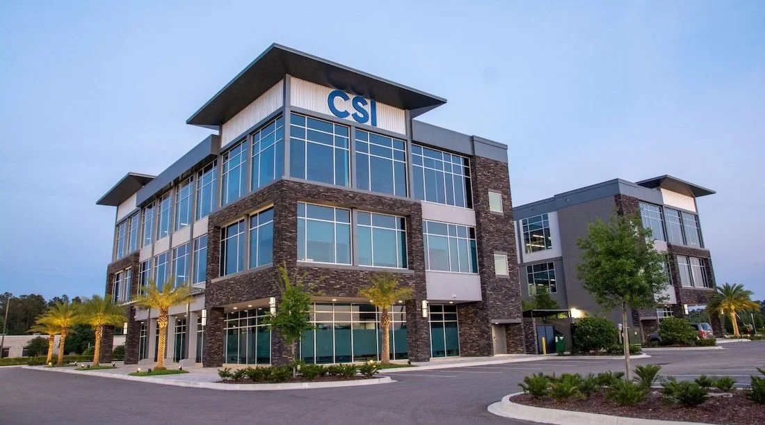 Modern CSI Companies headquarter building, with tall glass windows wrapped around and palm trees surrounding. Located in Jacksonville, Florida.