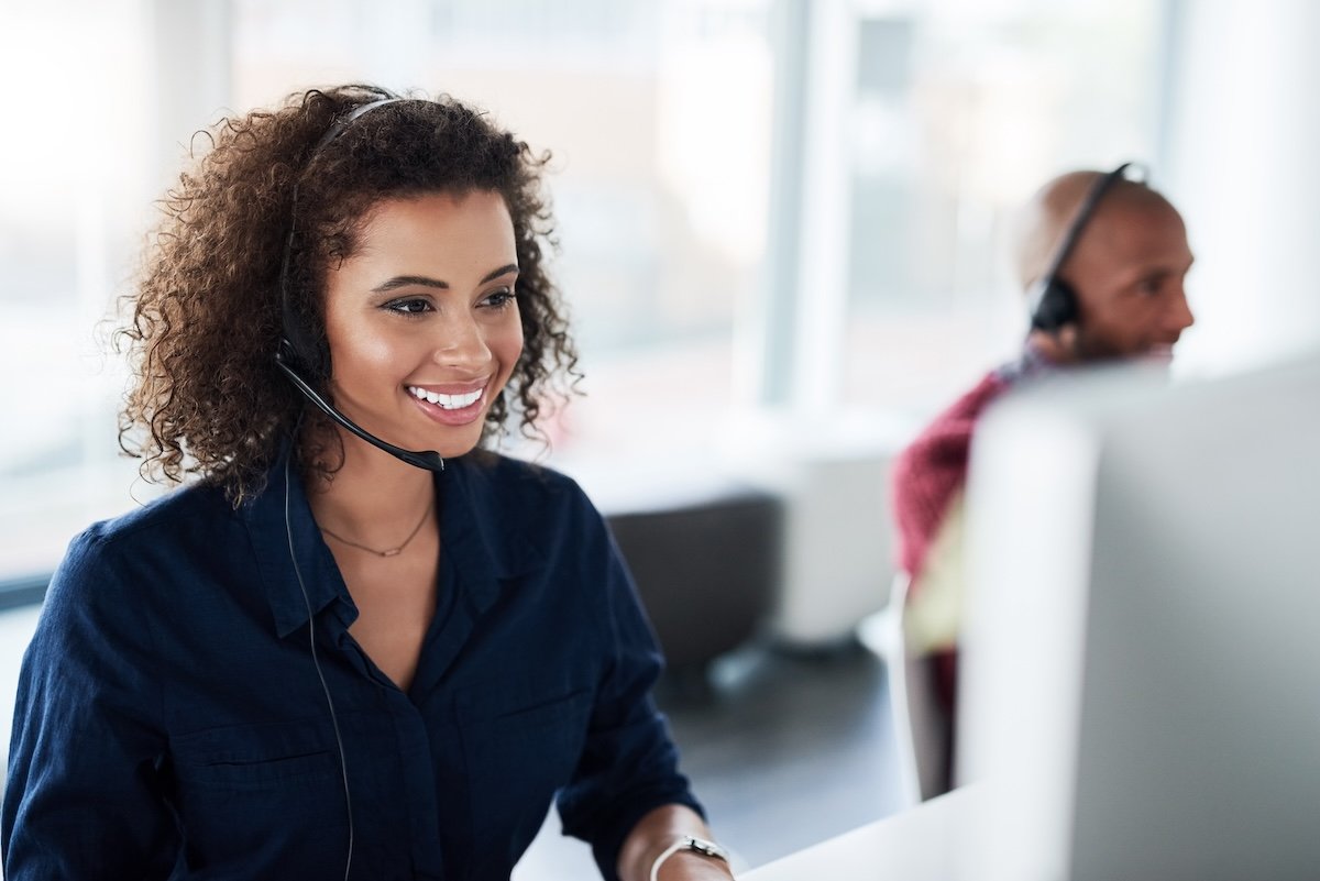 Woman with headset on at a call desk center, happily answering calls for technical services