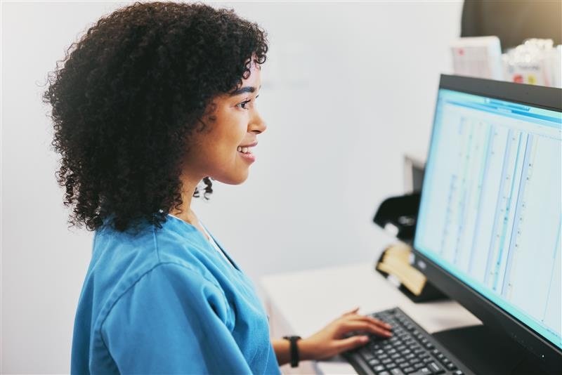 Nurse sitting at desk typing on desktop, reviewing patient charts.