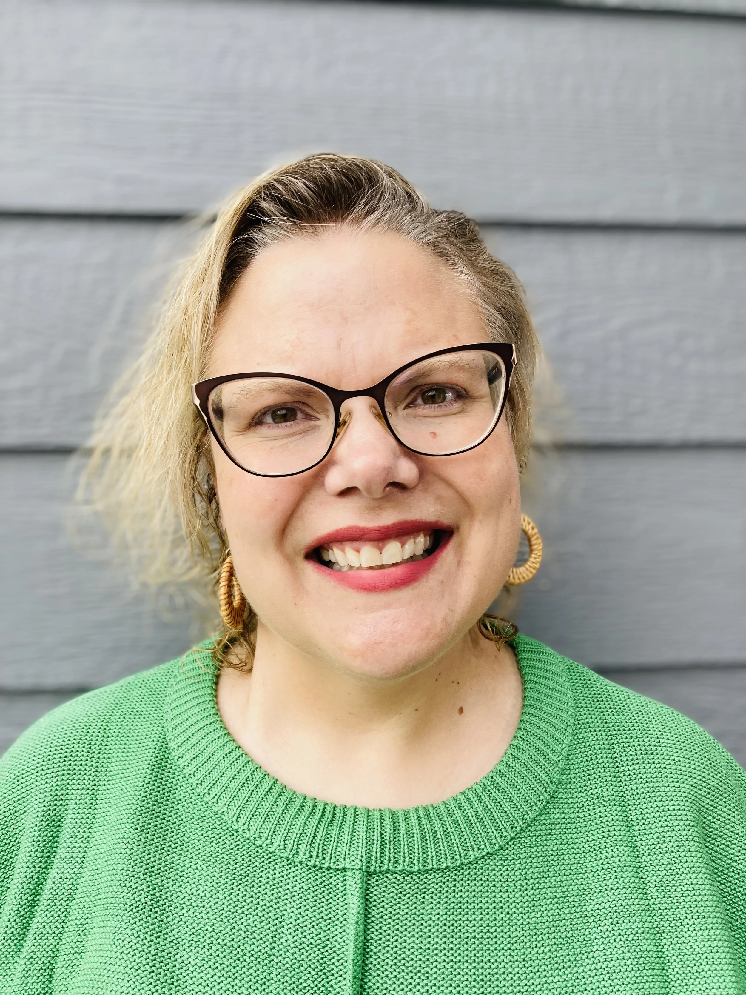 a woman with blonde hair, glasses, and red lipstick smiling at the camera