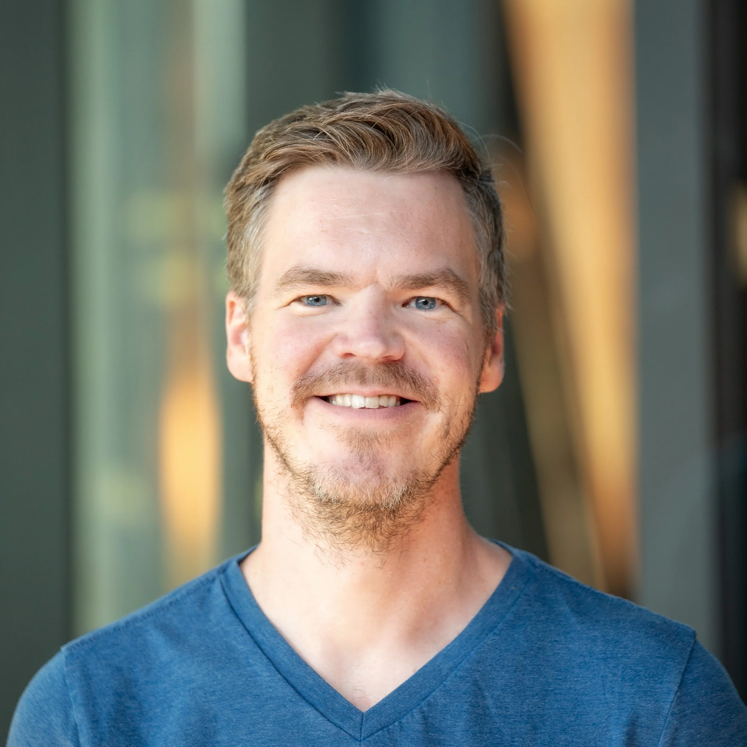 a young man with blue eyes and a beard smiling at the camera