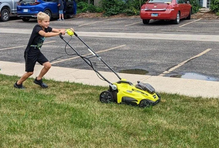 A volunteer pushes a battery-powered lawn mower across the grass