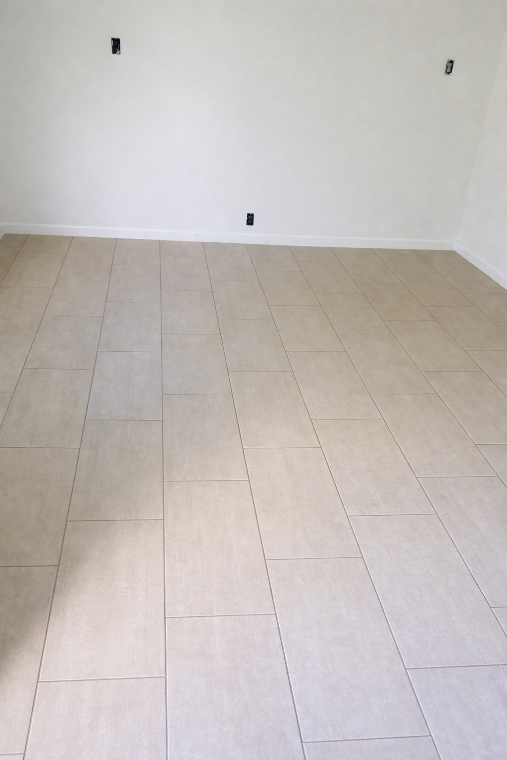 Empty room with beige tiled flooring, plain white walls, and electrical outlets without cover plates.