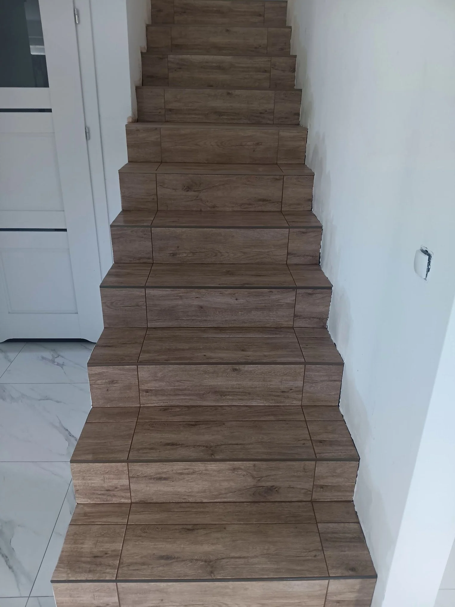 Interior of a staircase with wooden steps and a white wall on the right side, partially under construction or renovation.