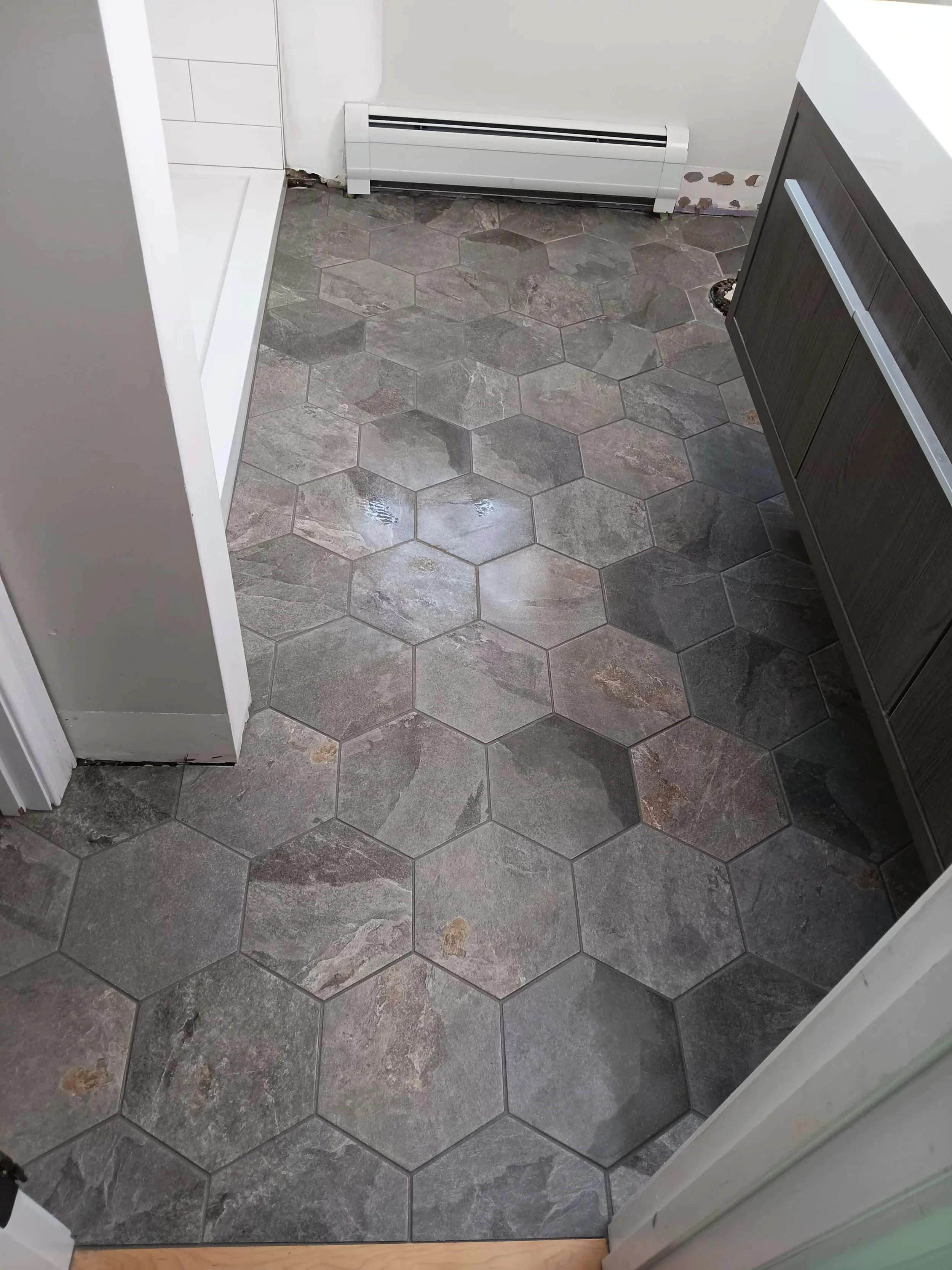 Floor with hexagonal stone tiles, part of a doorway, a radiator against a wall, and a section of a bathroom vanity.