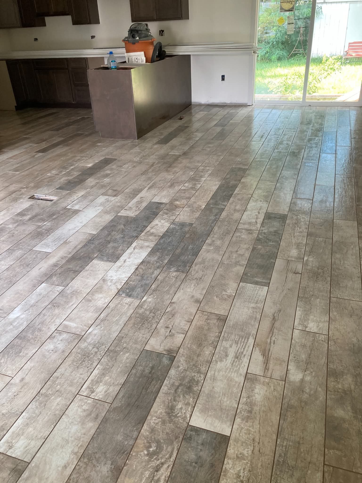 A partially renovated kitchen with wood-look tile flooring, dark wood cabinetry, and a sliding glass door leading to the backyard.