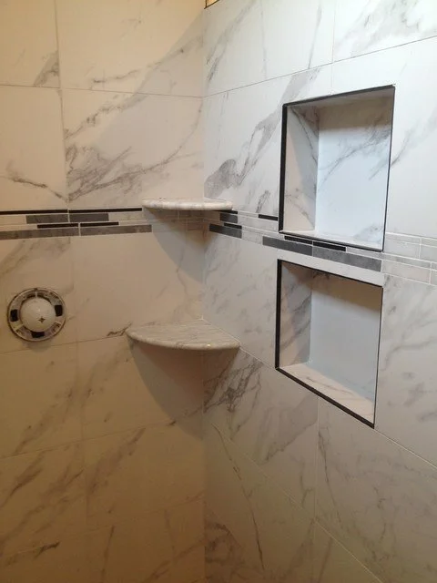 A marble-tiled shower wall with two built-in wall niches and two corner shelves.