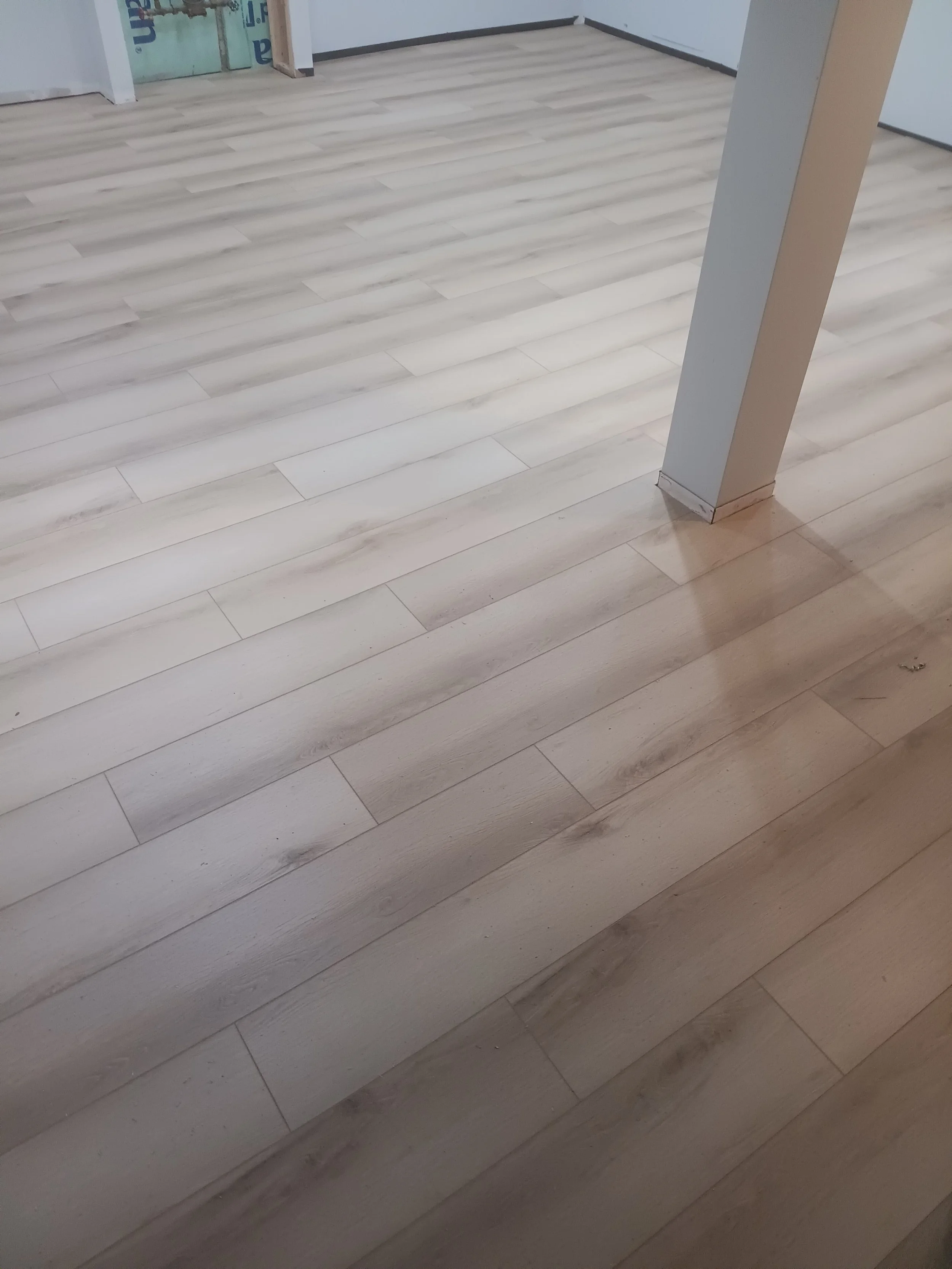 Interior space with light-colored wooden flooring, a white wall with a partial doorway, and an angled support column.