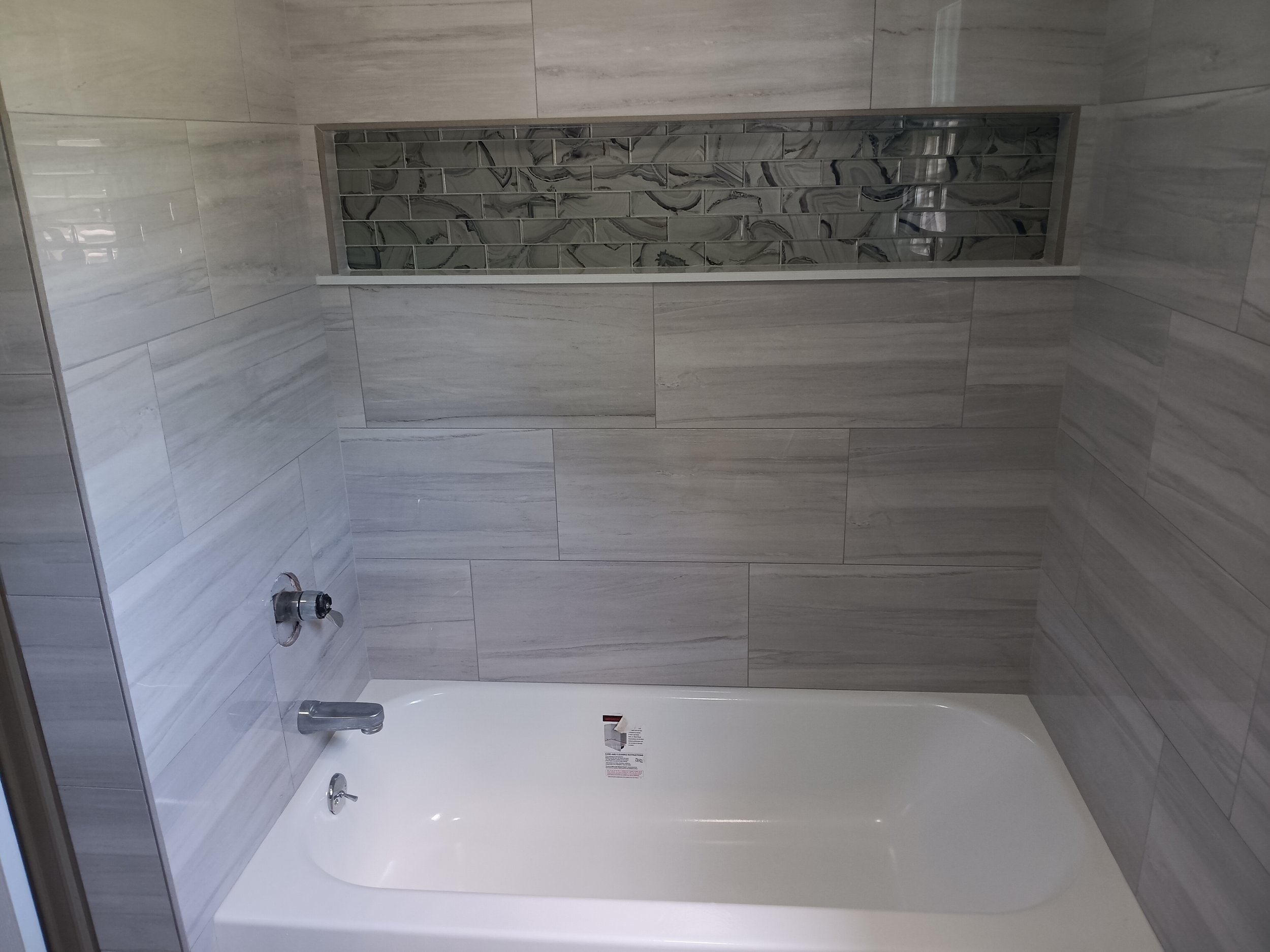 A shower with a built-in niche featuring marble-patterned tile, surrounded by large rectangular grey tiles.