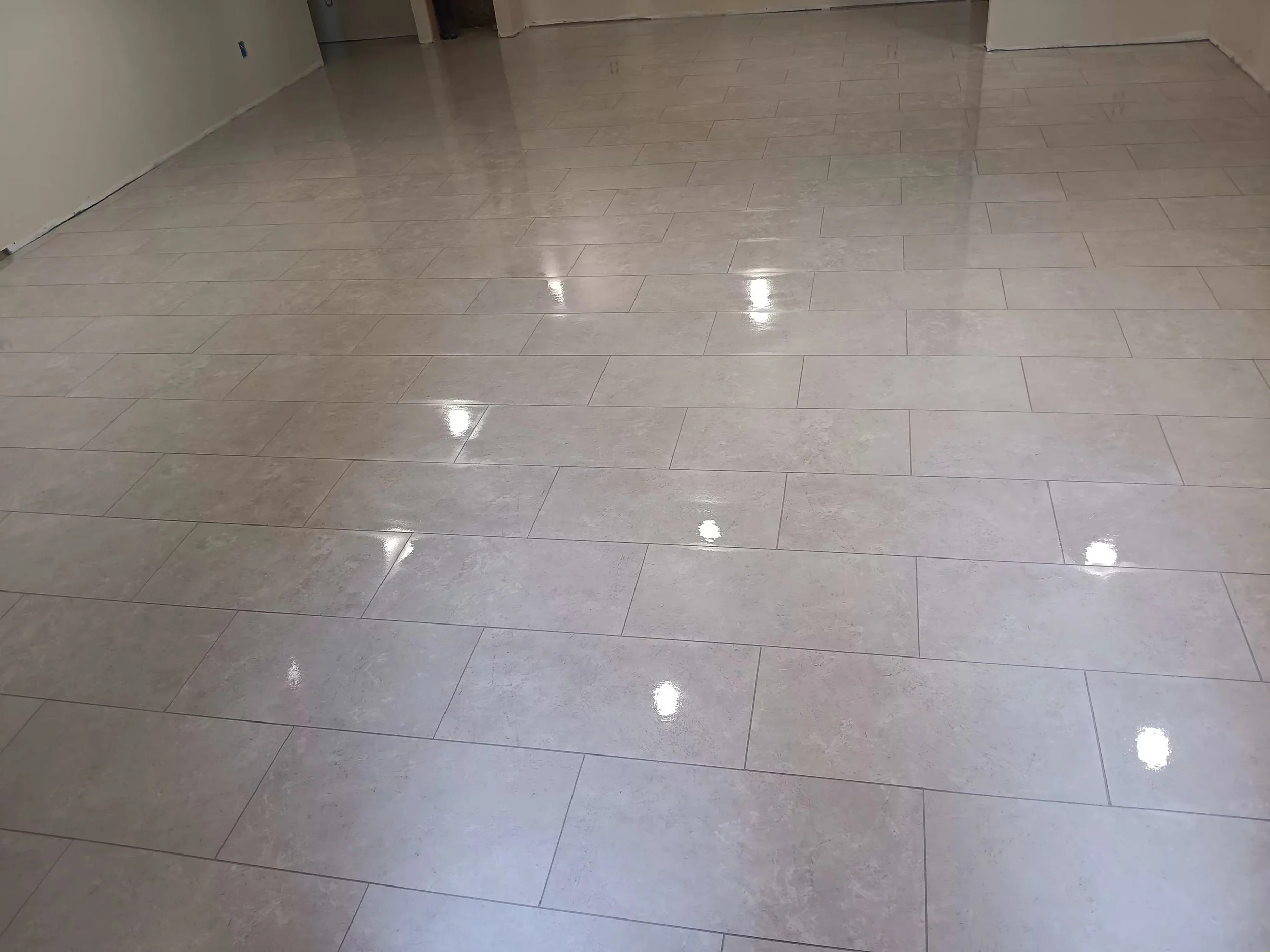 Shiny beige tiled floor in an indoor space, with reflections from ceiling lights