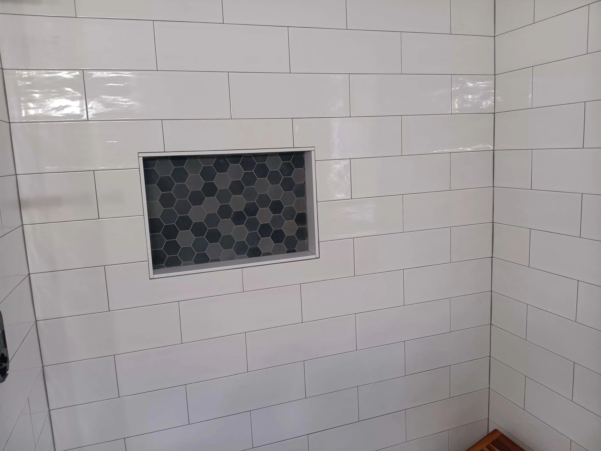 A white tiled interior wall with rectangular tiles and a recessed shelf with a black hexagon patterned tile background.