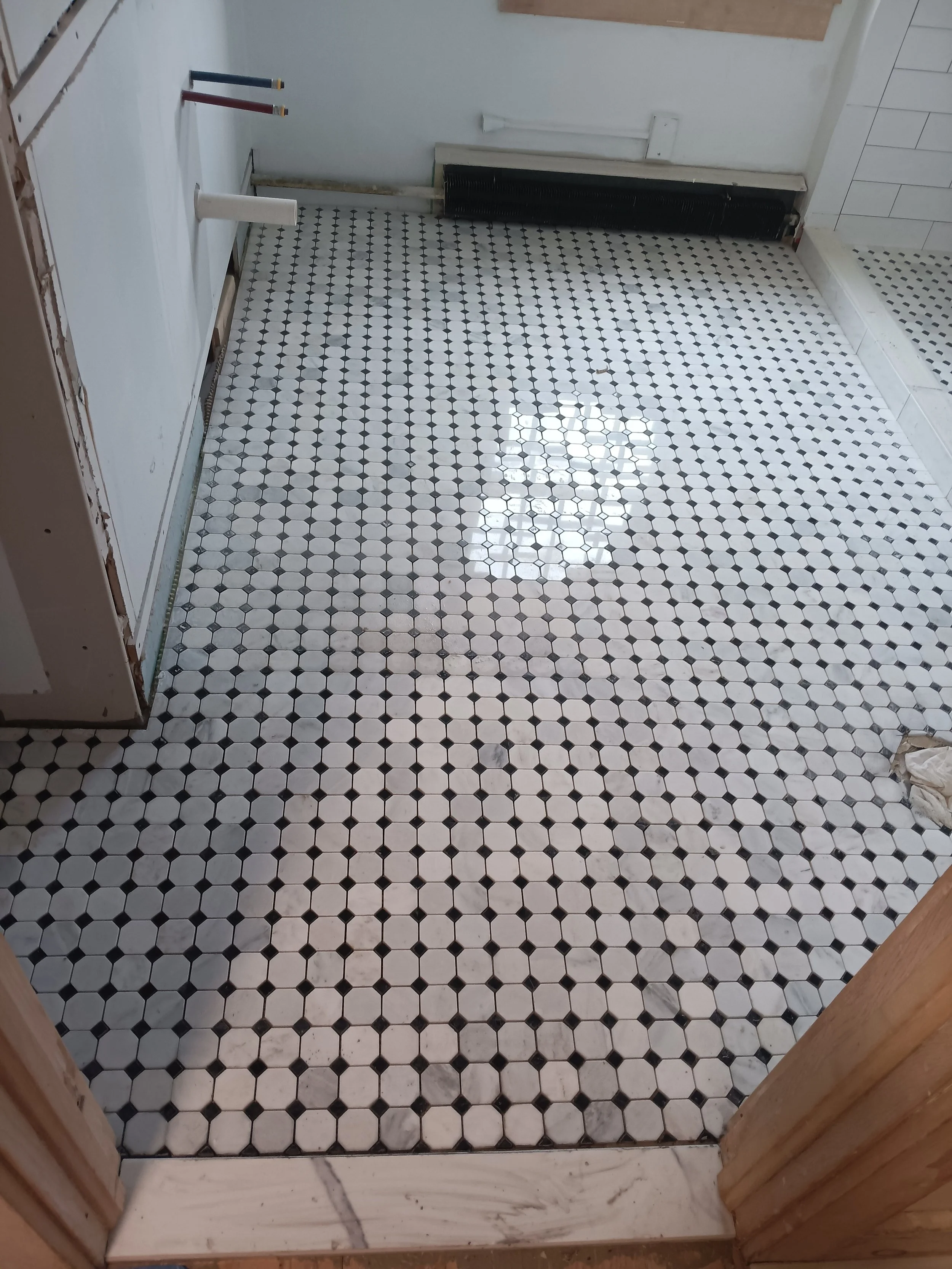 A partially finished bathroom with black and white hexagon tile flooring, white walls, and some construction materials and tools visible.