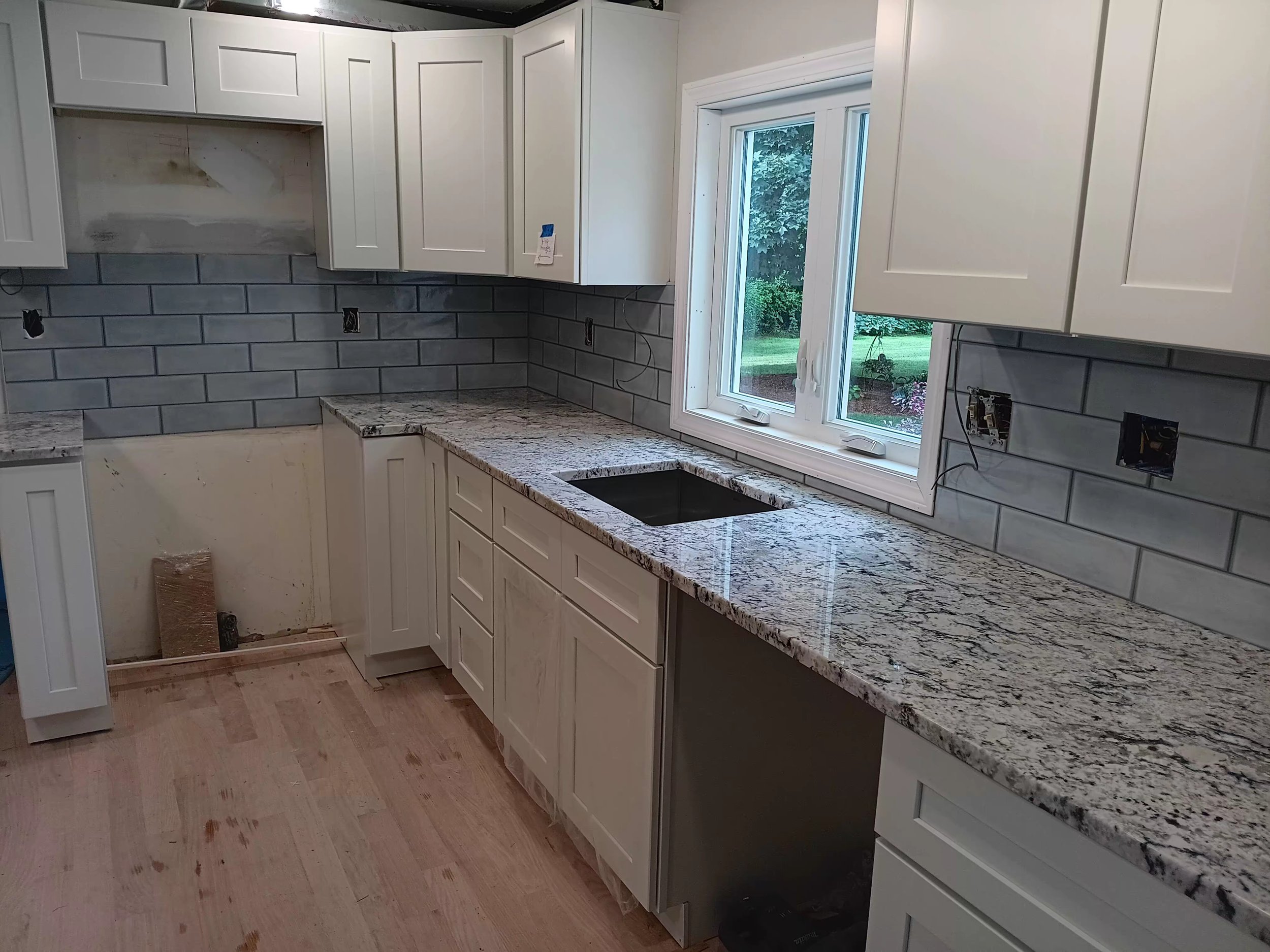 Kitchen under renovation with white cabinets, granite countertops, grey subway tile backsplash